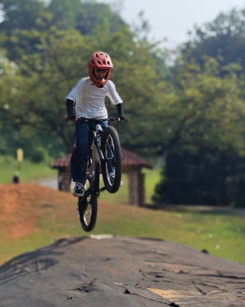 Armand launching a jump on his Marin hardtail, wearing a red full-face helmet, white shirt, and jeans